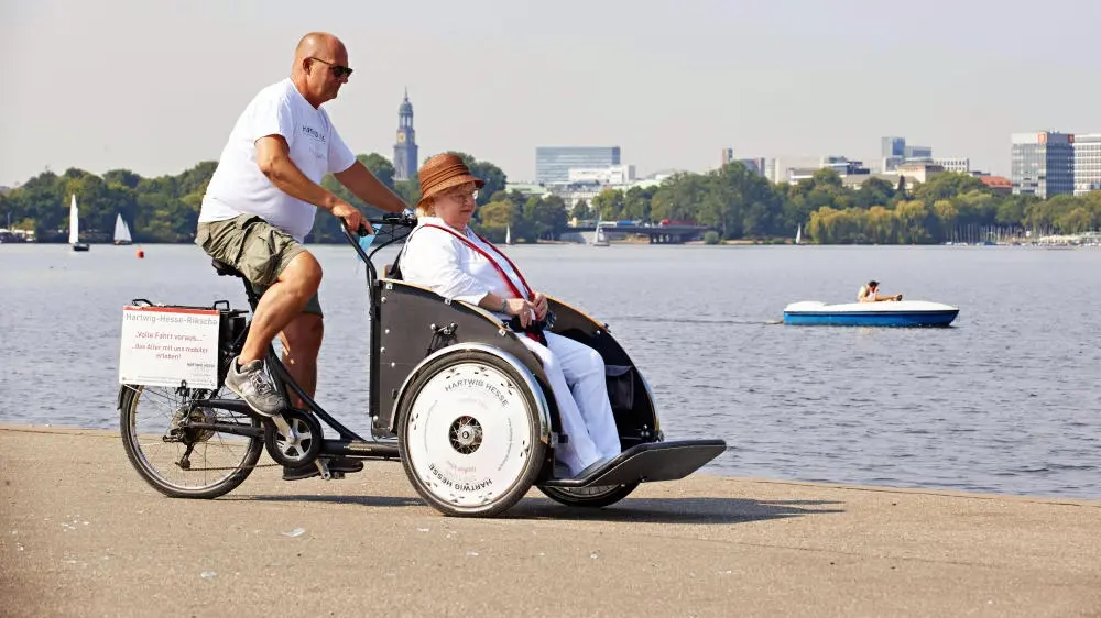 Pflegefachkraft unternimmt mit einer Seniorin einen Ausflug mit dem Lastenrad