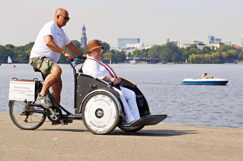 Pflegefachkraft unternimmt mit einer Seniorin einen Ausflug mit dem Lastenrad