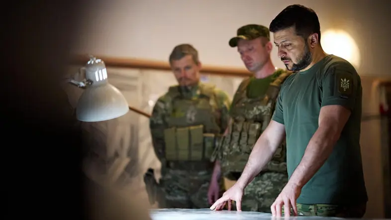 Wolodymyr Selenskyi und zwei Soldaten blicken konzentriert auf Unterlagen