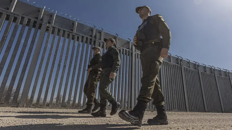 Zu sehen sind drei Soldaten, die einen großen Zaun entlanggehen. 