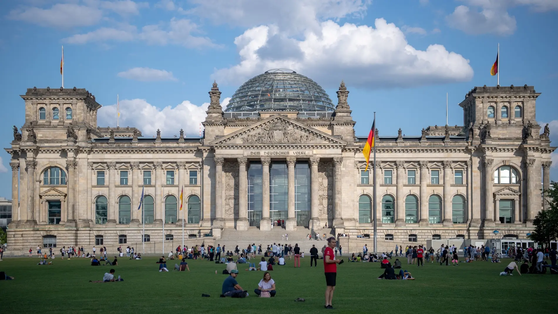 Touristen sitzen vor dem Reichstagsgebäude auf der Treppe und dem Rasen