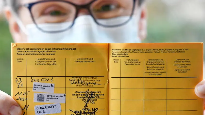 Gestempelter Impfpass wird von Person mit Brille und medizinischer Maske gehalten