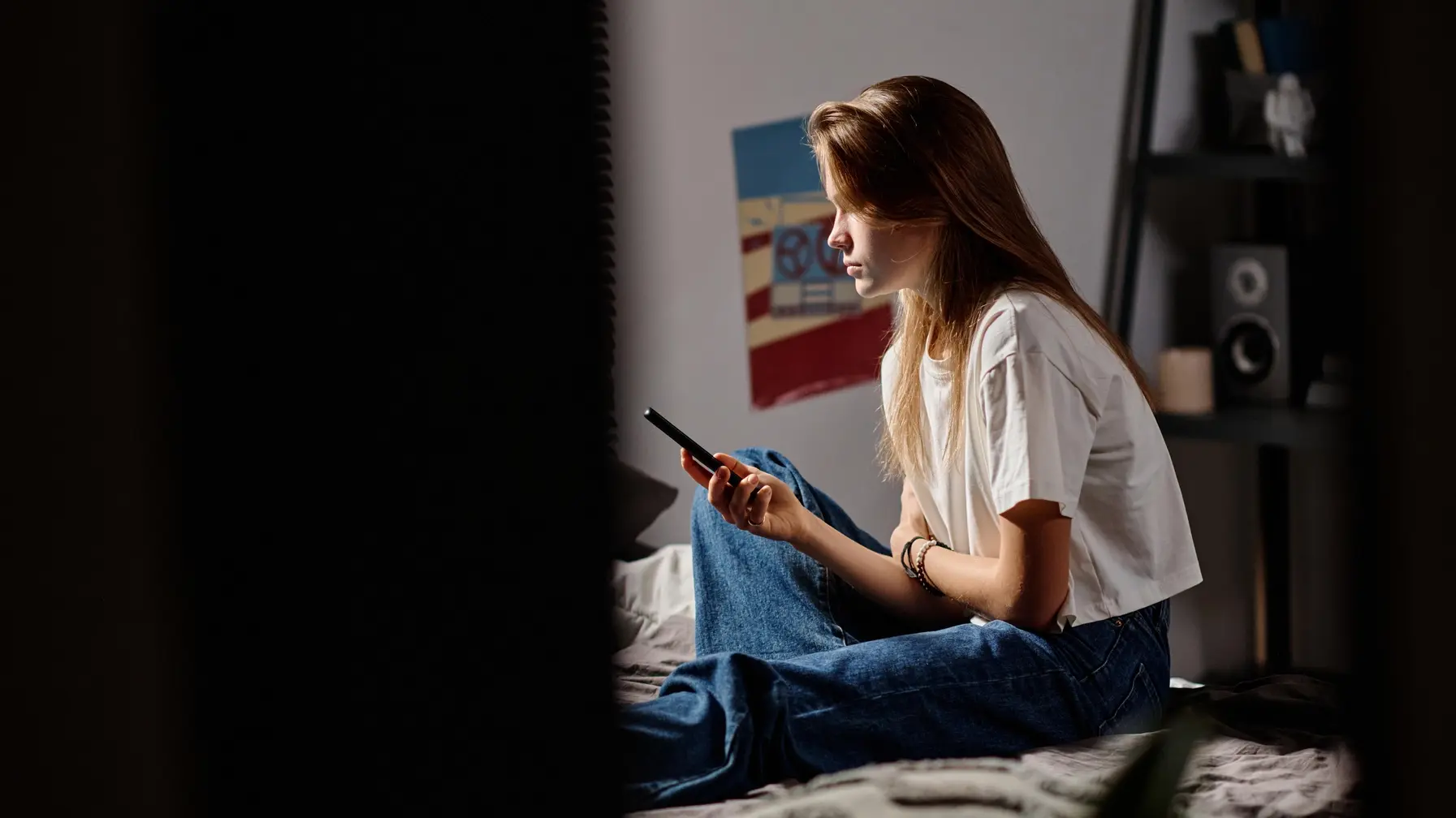 Eine Teenagerin sitzt auf dem Bett und schaut auf ihr Smartphone.