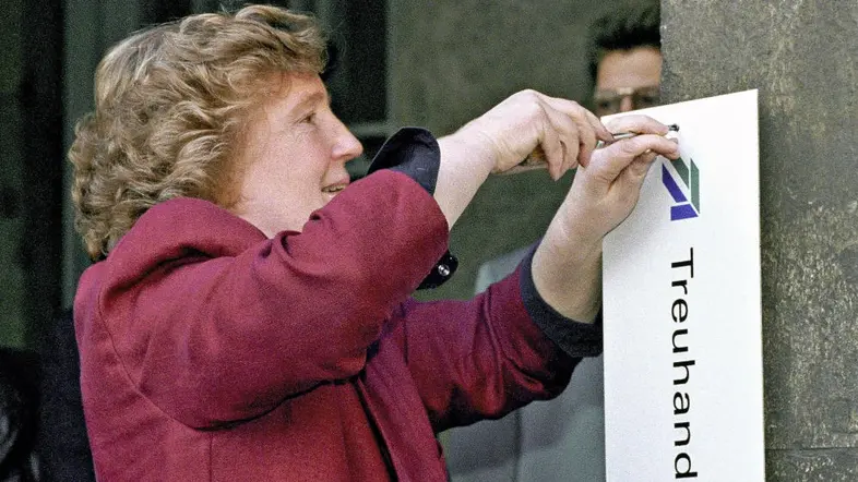 Birgit Breul im roten Blazer schraubt das Schild der Berliner Treuhand-Zentrale ab.