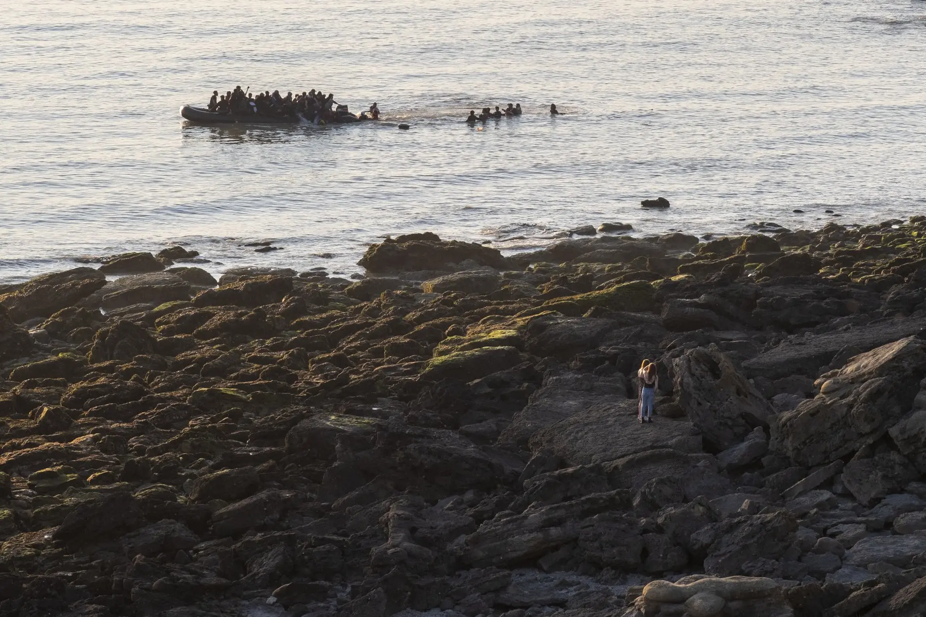 Zu sehen ist ein Schlauchboot mit vielen Menschen, das am frühen Morgen von einem Ufer auf das Meer fährt. 