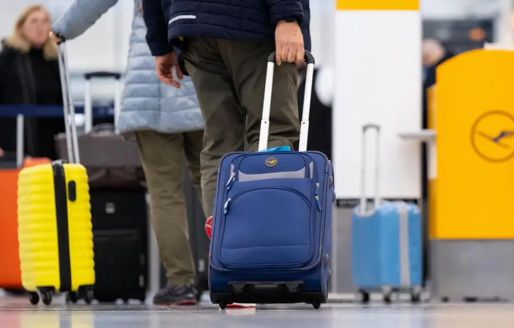 EU-einheitliche Handgepäckregelung Passagiere stehen mit ihrem Handgepäck am Check-in-Schalter vom Flughafen.