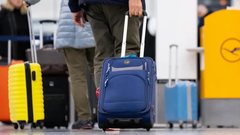 Passagiere stehen mit ihrem Handgepäck am Check-in-Schalter vom Flughafen.
