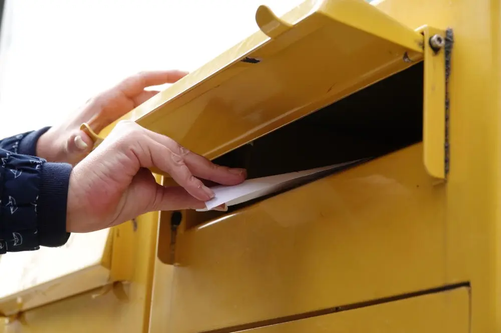 Postkarte wird in einen Briefkasten geworfen Postkarte wird in einen Briefkasten geworfen