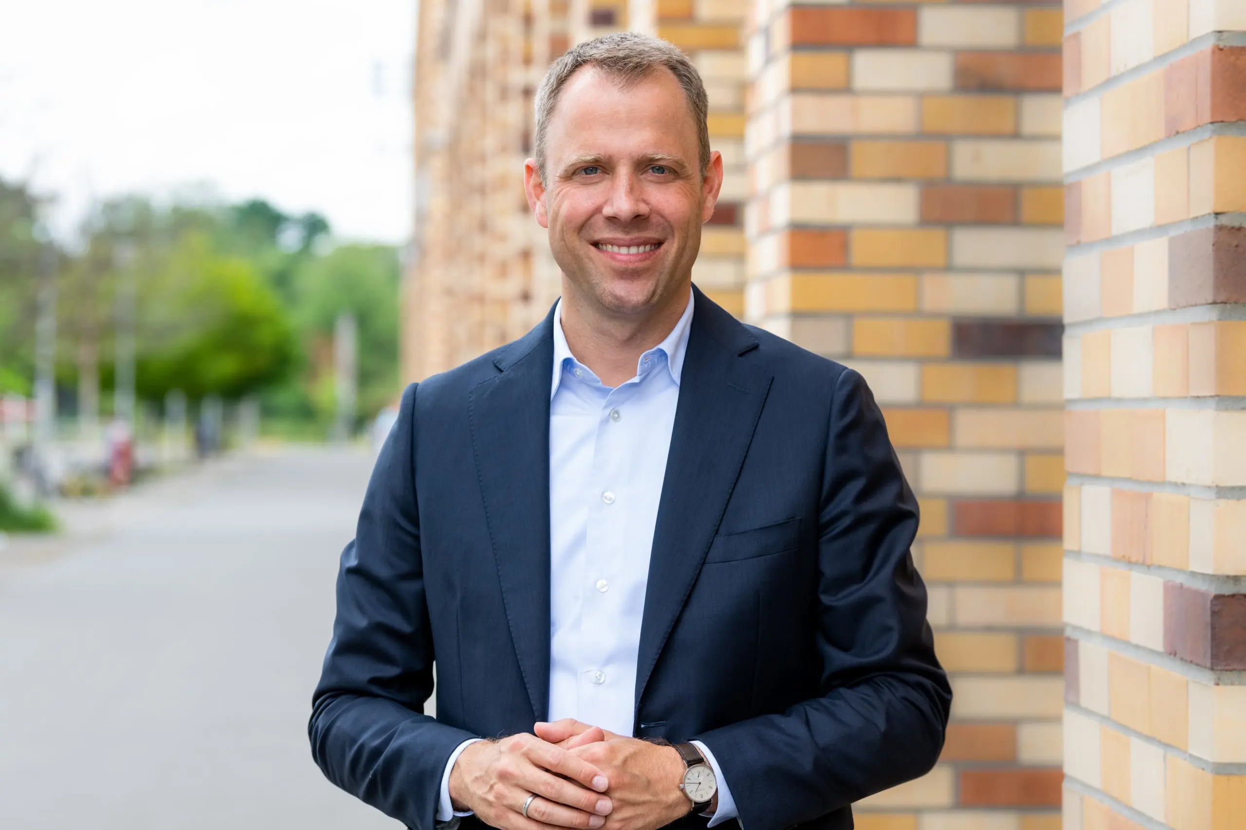 Mario Czaja lächelnd im Anzug vor einer Mauer.