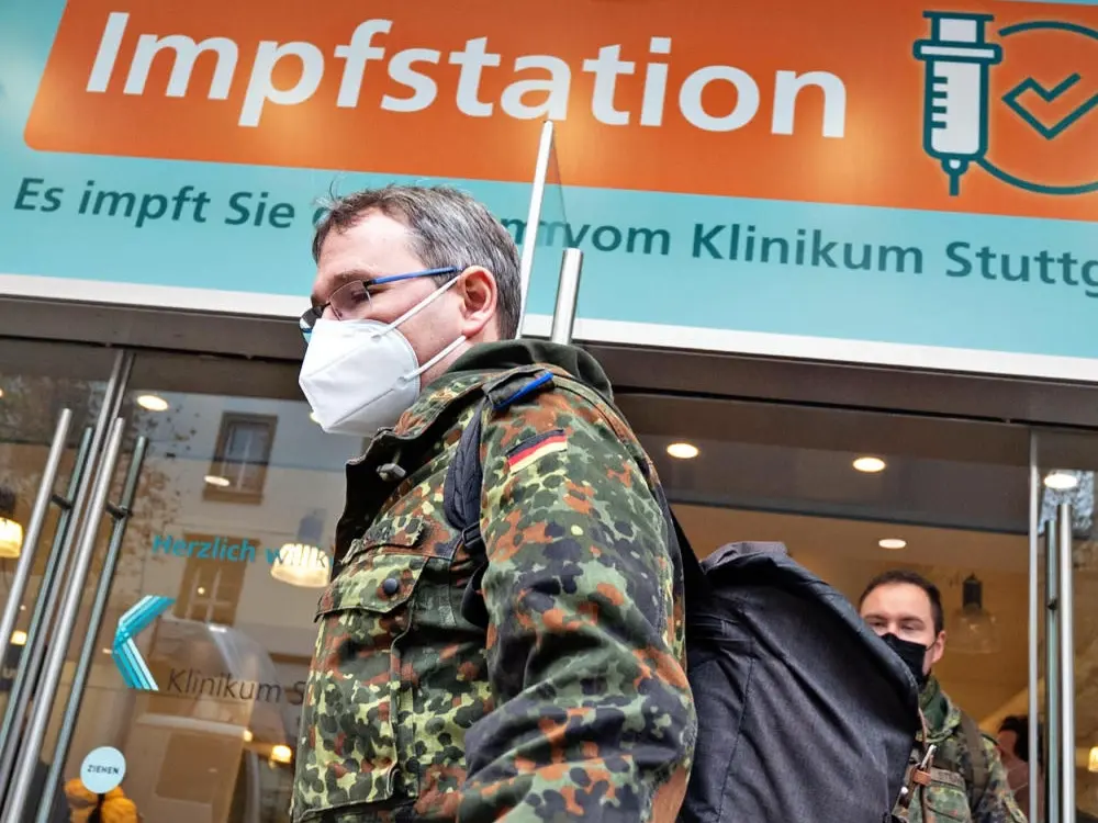 Das Bild zeigt einen Soldaten mit Maske vor einer Impfstation.