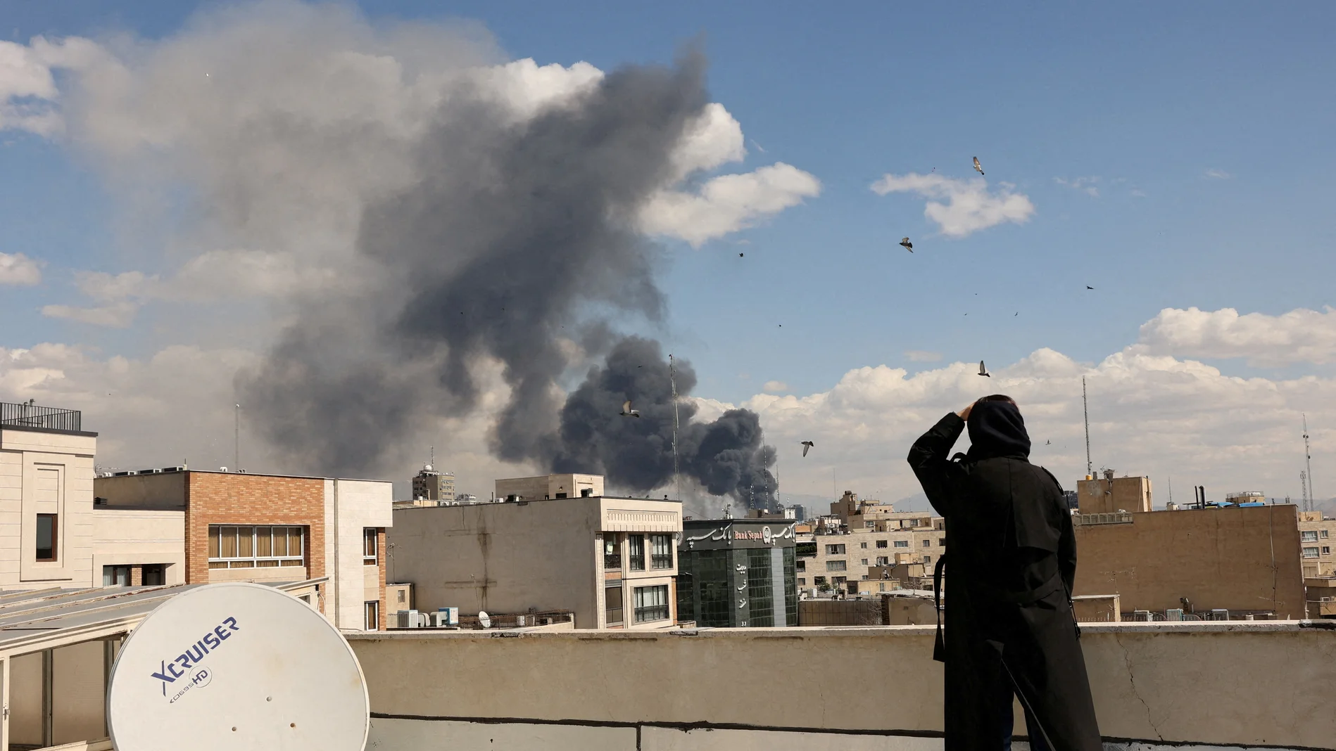 Eine Person blickt vom Dach eines Hauses auf eine Explosion in Teheran