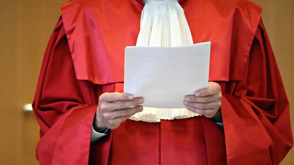 Bundesverfassungsgericht Mann in roter Robe hält einen Stapel Papier