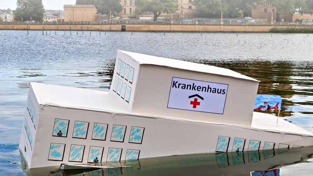 Das Bild zeigt ein Papp-Krankenhaus, welches im Wasser untergeht.