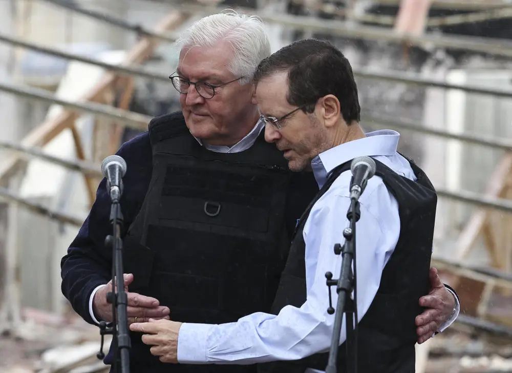 Bundespräsident Steinmeier und Israels Präsident Herzog im zerstörten Kibbuz Be'eri. Bundespräsident Steinmeier und Israels Präsident Herzog stehen mit Schutzwesten bekleidet vor einem zerstörten Haus.