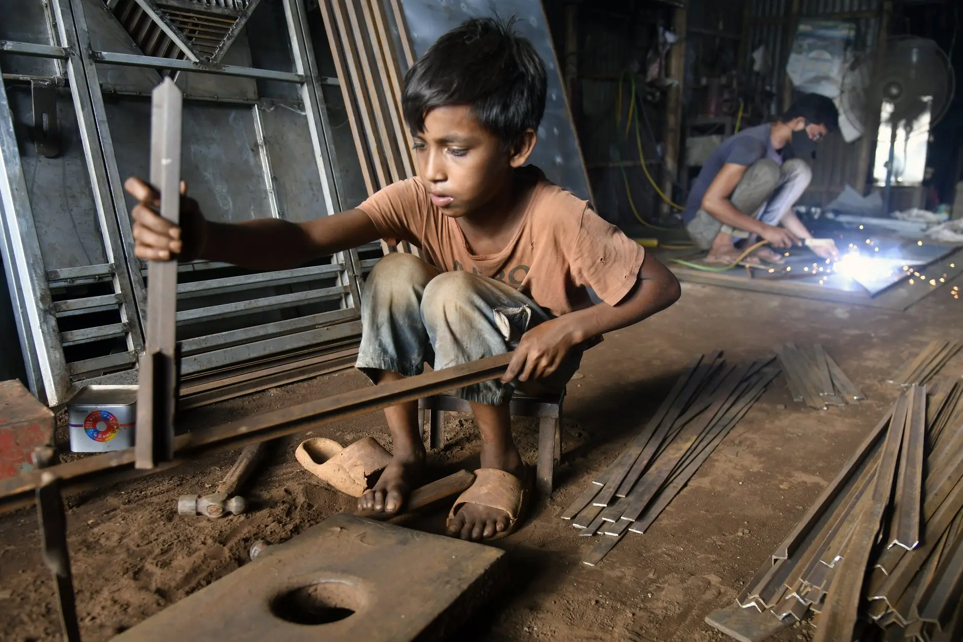 Ein kleiner Junge sitzt in einer Metallwerkstatt in Bangladesh und arbeitet.