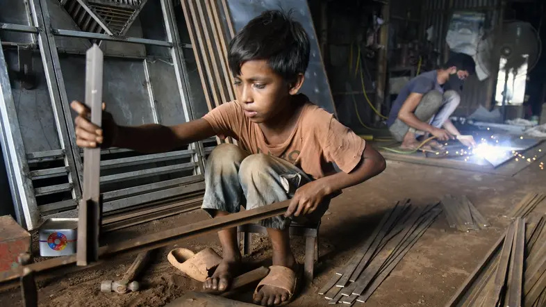 Ein kleiner Junge sitzt in einer Metallwerkstatt in Bangladesh und arbeitet.