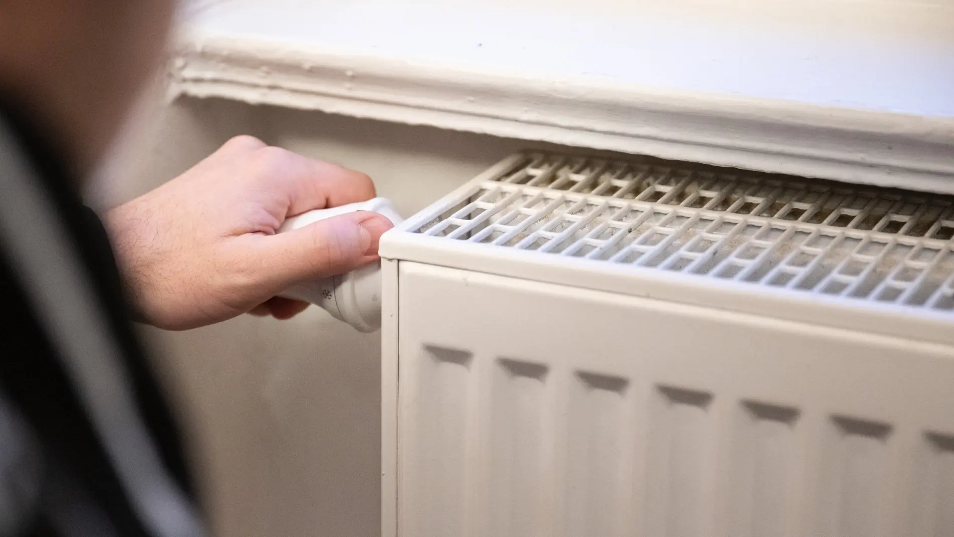Mann dreht am Thermostat einer Heizung Mann dreht am Thermostat einer Heizung