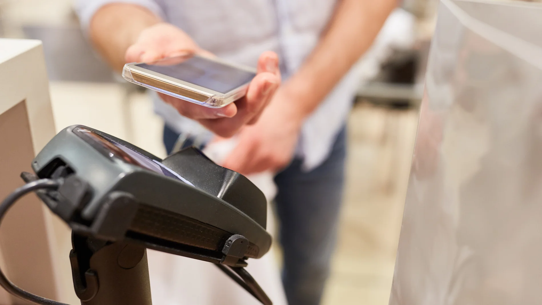 Kunde bezahlt mit NFC Smartphone am Kartenterminal Kasse im Shoppingcenter