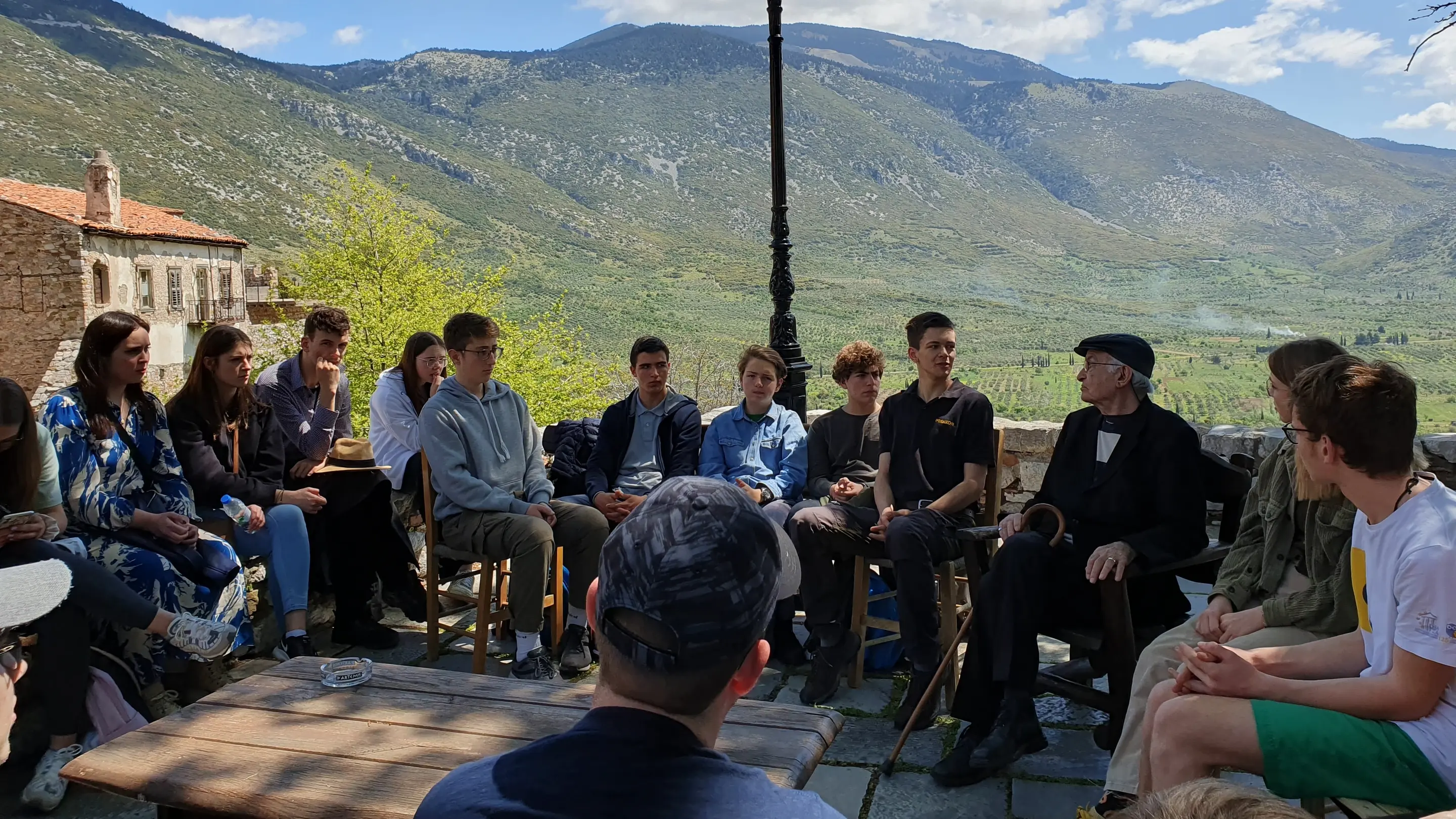 Zeitzeugengespräch mit Argyris Sfountouris Eine Gruppe Menschen sitzt vor einer bergigen Kulisse