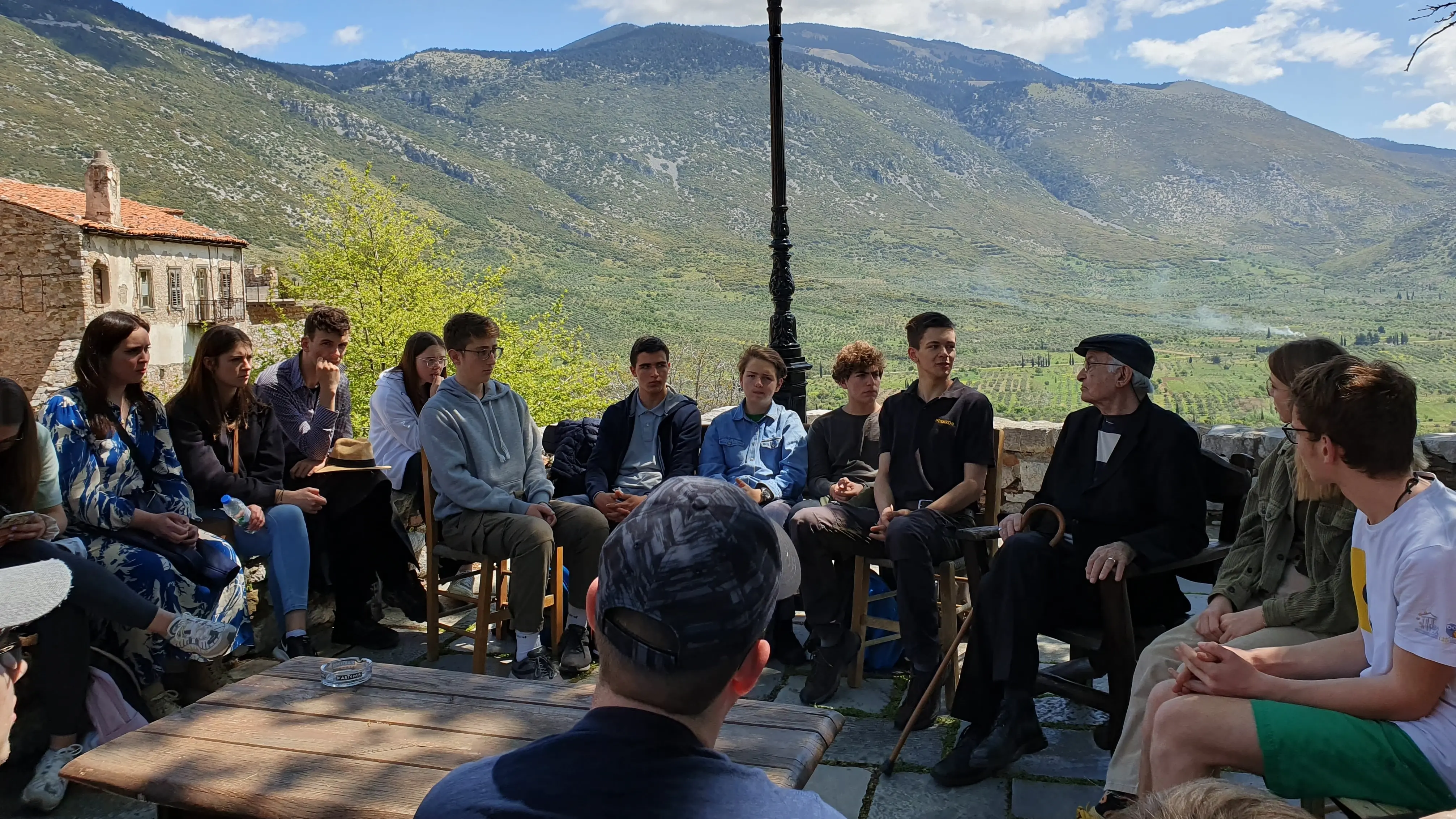 Zeitzeugengespräch mit Argyris Sfountouris Eine Gruppe Menschen sitzt vor einer bergigen Kulisse