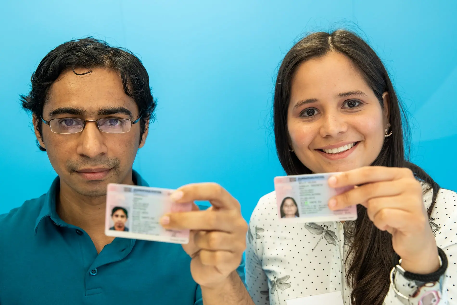 Elektroingenieurin aus Venezuela und Softwareentwickler aus Indien halten ihre "Blaue Karte" in den Händen.