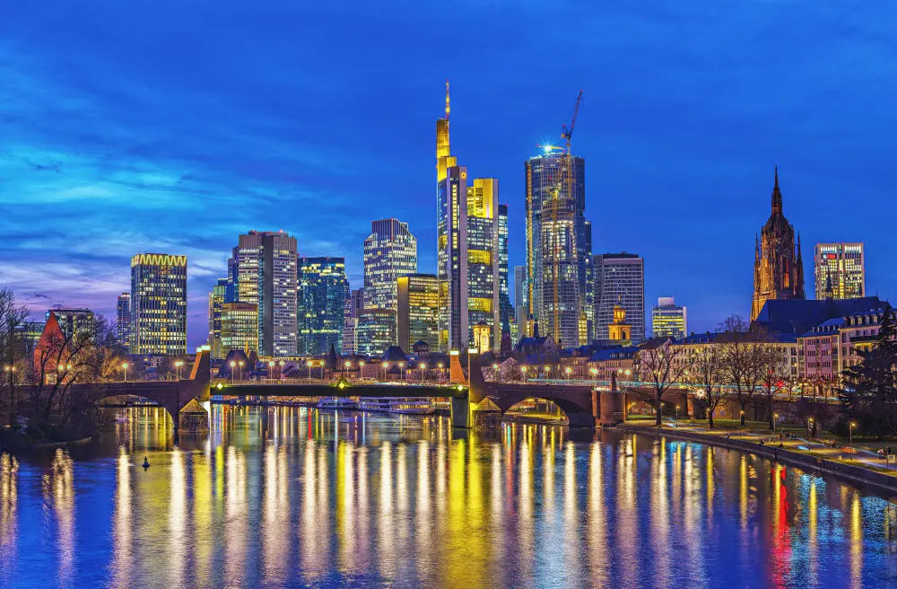 Kapitalmarkt für Altersvorsorge Die Frankfurter Skyline hinter dem Main zur blauen Stunde nach Sonnenuntergang.