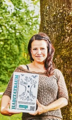 Daniela Antoni hält ein Zertifikat in der Hand und steht vor einem Baum