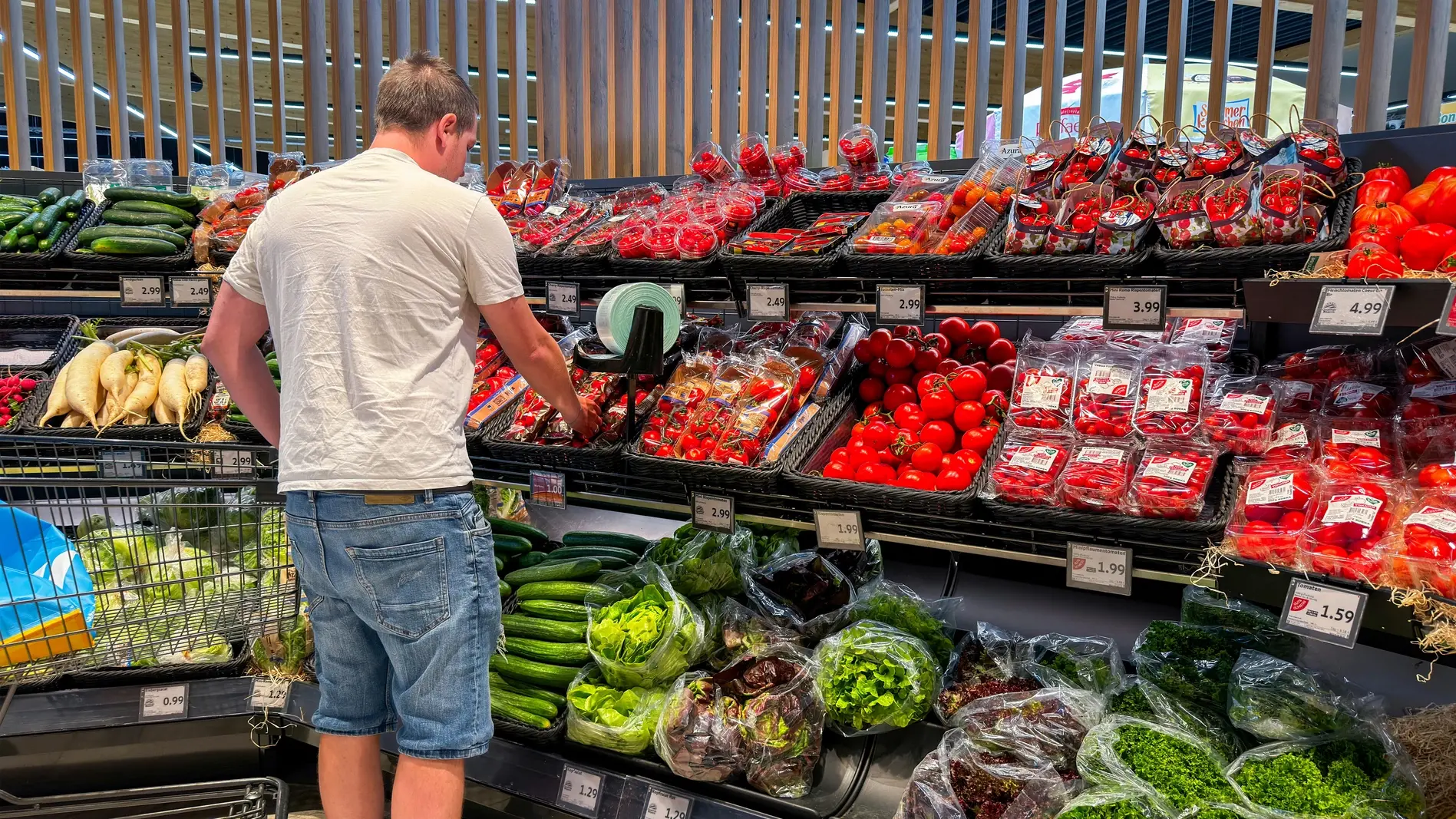 Ein Mann steht im Supermarkt an der Gemüseabteilung