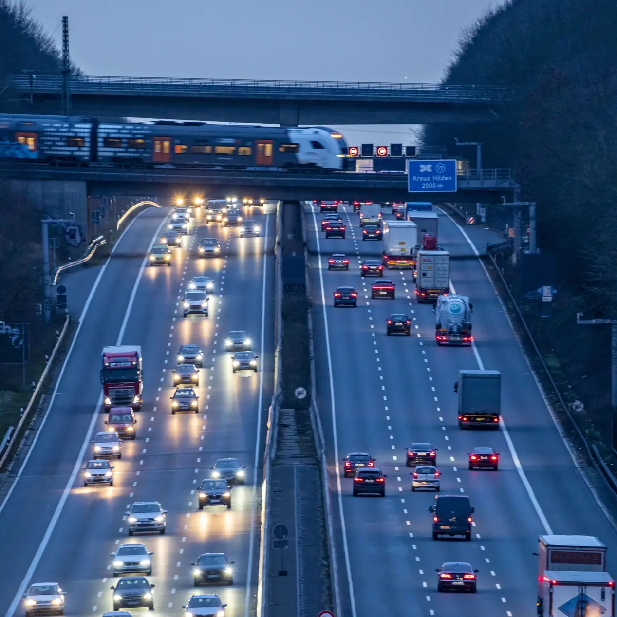 Emissionsfreie Fahrzeuge ab 2035 Abendlicher Berufsverkehr auf der A3. Ein Nahverkehrszug überquert die Autobahnbrücke.