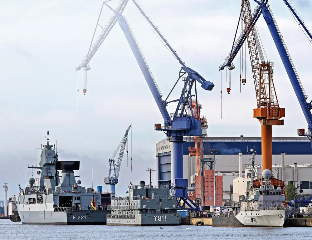 Drei Fregattenschiffe im Hafen, im Hintergrund sind mehrere Kräne.