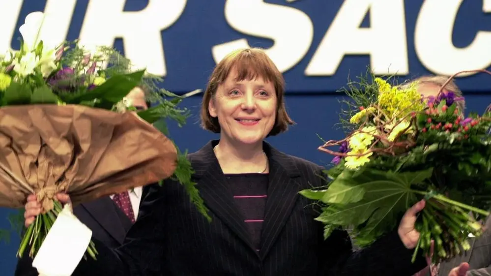 Mit zwei Blumensträußen in der Hand lächelt Angela Merkel