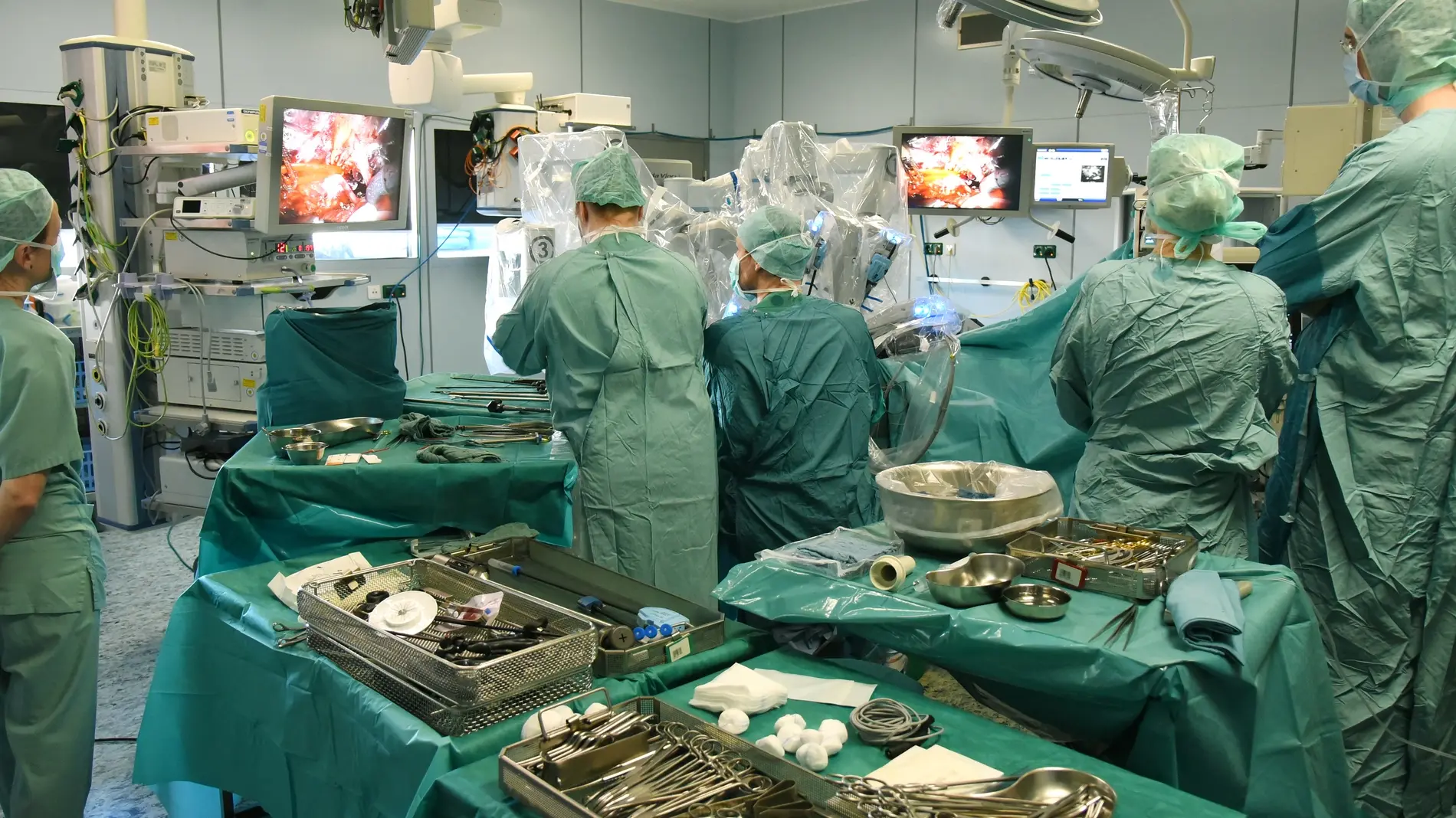 Blick in einen OP-Saal, viele Tische mit OP-Besteck und Menschen in grünen Roben