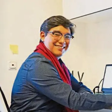 Julio Rodriguez lächelnd am Schreibtisch vor einem Laptop.