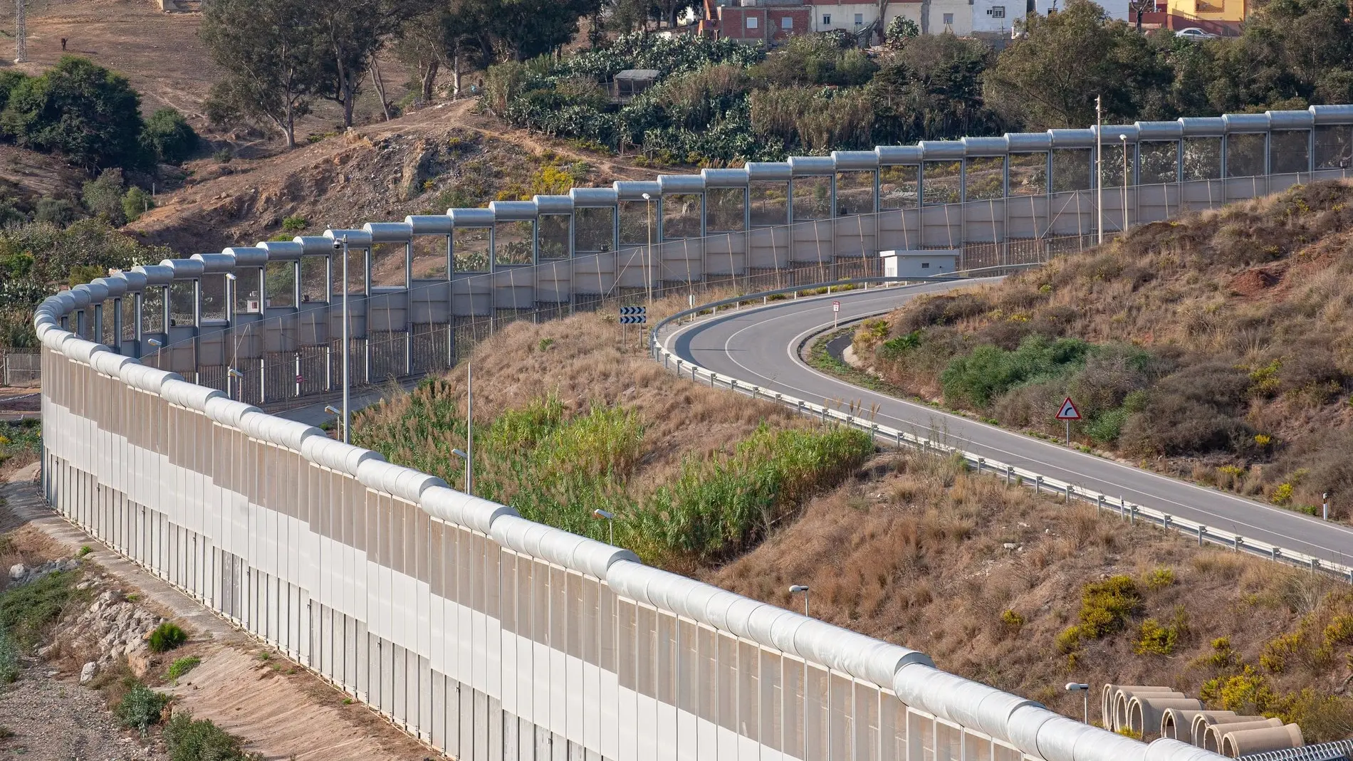 Grenzzaun zwischen Marokko und der EU-Enklave Ceuta Zu sehen ist eine lange Mauer neben einer Straße.