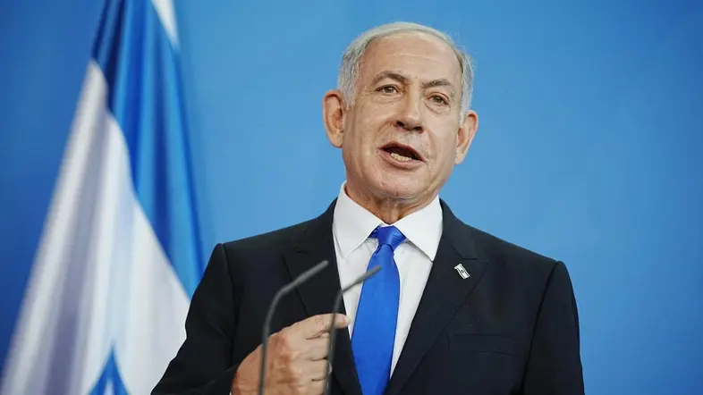 Benjamin Netanjahu steht vor einem Mikrofon, hinter ihm eine israelischen Fahne.