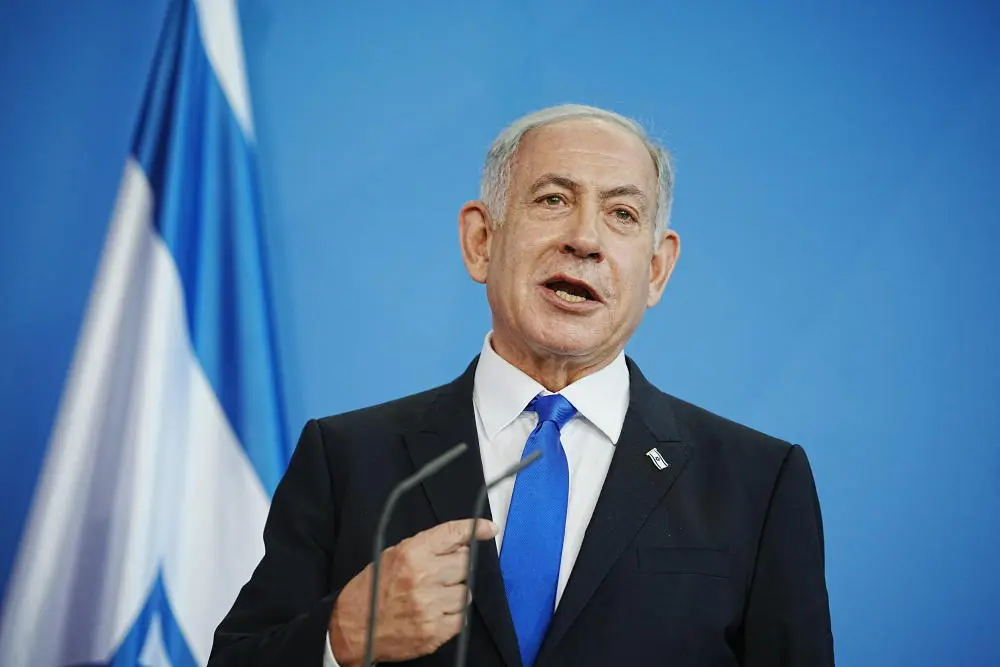 Benjamin Netanjahu steht vor einem Mikrofon, hinter ihm eine israelischen Fahne.