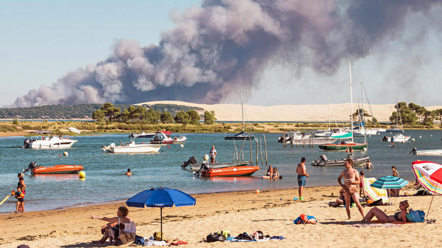 Strandbesucher; zahlreiche Boote, ein heftiger Waldbrand im Hintergrund.