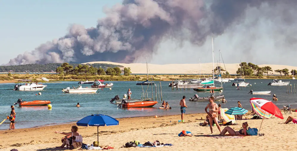 Strandbesucher; zahlreiche Boote, ein heftiger Waldbrand im Hintergrund.