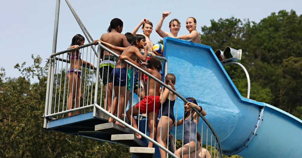 Zu sehen sind Kinder im Freibad auf einer Wasserrutsche.