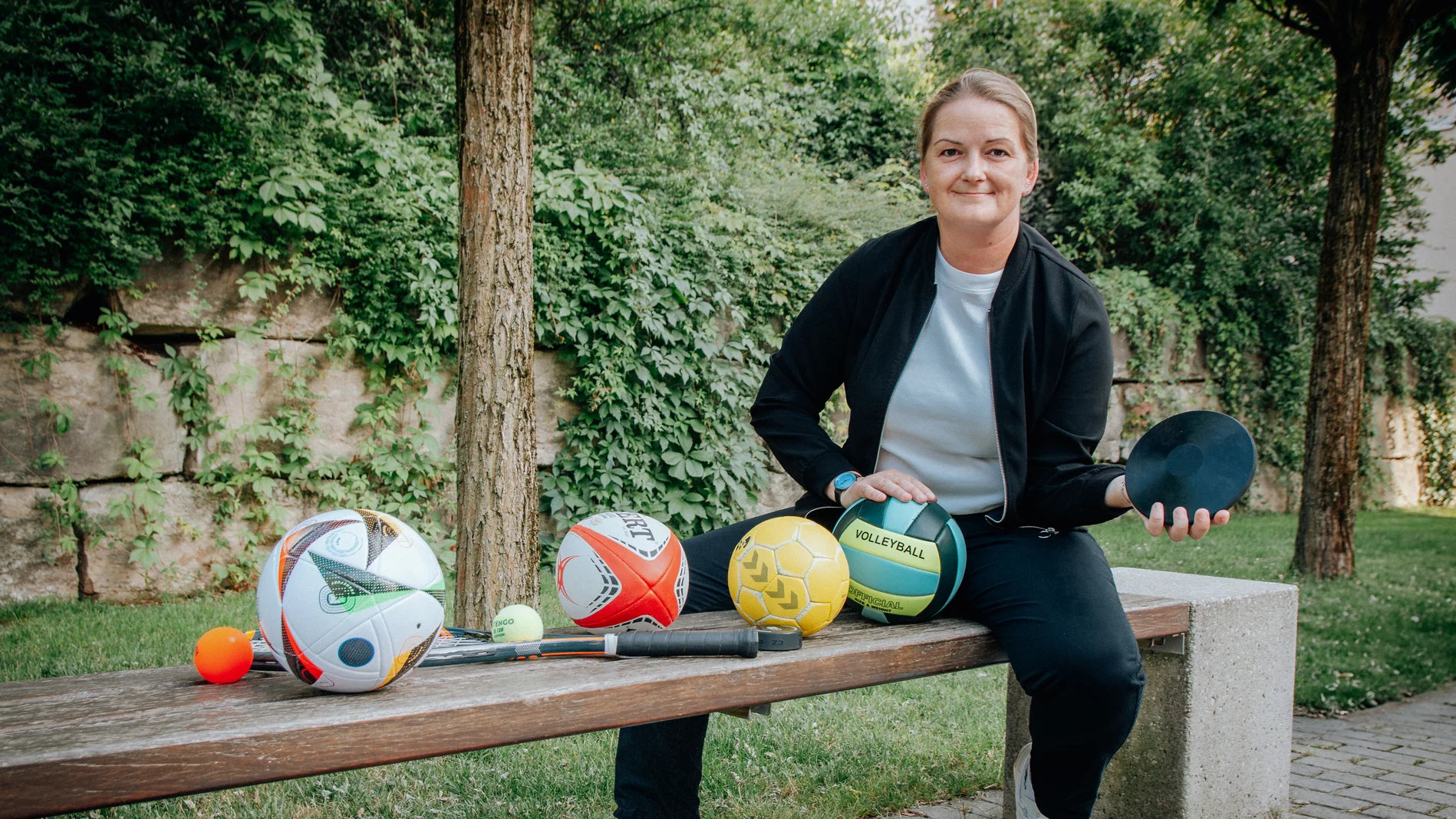 Tina Winklmann posiert auf einer Bank mit verschiedenen Sportbällen
