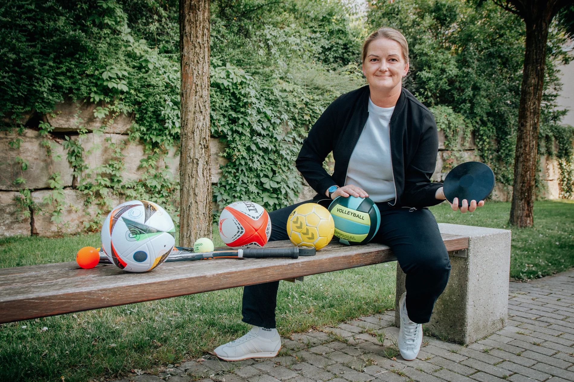 Tina Winklmann posiert auf einer Bank mit verschiedenen Sportbällen
