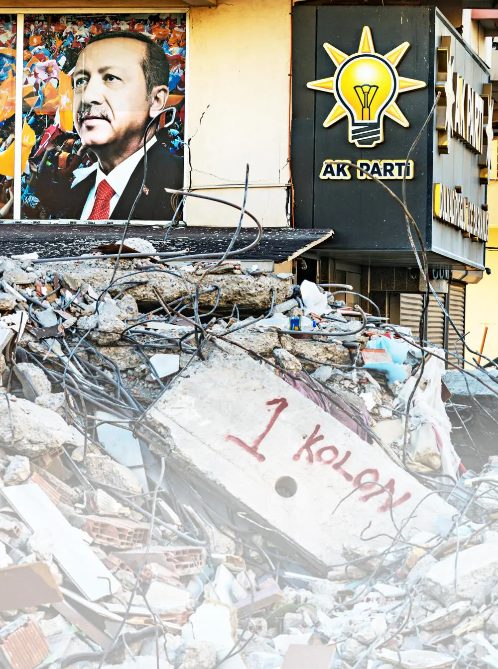 Trümmer eines eingestürzten Hauses, im Hintergrund hängt ein Wahlplakat Erdogans