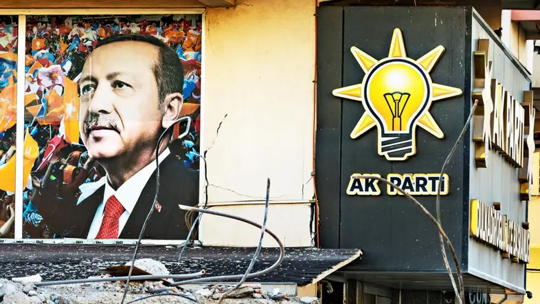Trümmer eines eingestürzten Hauses, im Hintergrund hängt ein Wahlplakat des türkischen Präsidenten Erdogans.