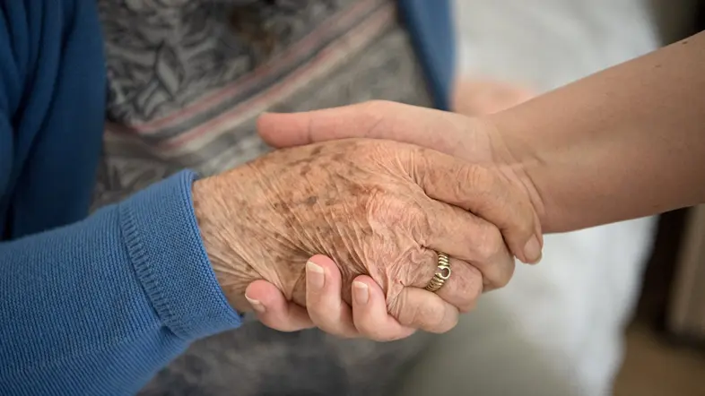 Eine Aufnahme einer Pflegekraft, die die Hand einer Seniorin hält