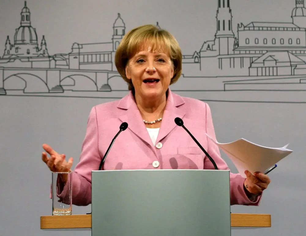Angela Merkel an einem Rednerpult im rosafarbenen Blazer