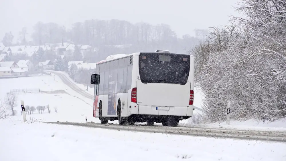 Regionalbus bei Schneegestöber und glatter Fahrbahn auf einer Landstraße.