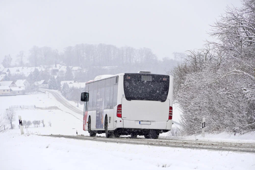 Regionalbus bei Schneegestöber und glatter Fahrbahn auf einer Landstraße.