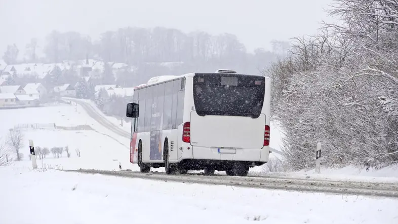 Regionalbus bei Schneegestöber und glatter Fahrbahn auf einer Landstraße.