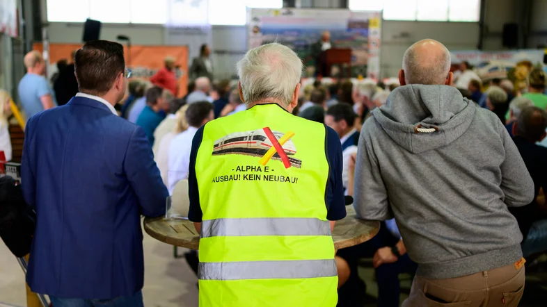 "Alpha E, Ausbau! Kein Neubau" steht auf einer Warnweste eines Mannes