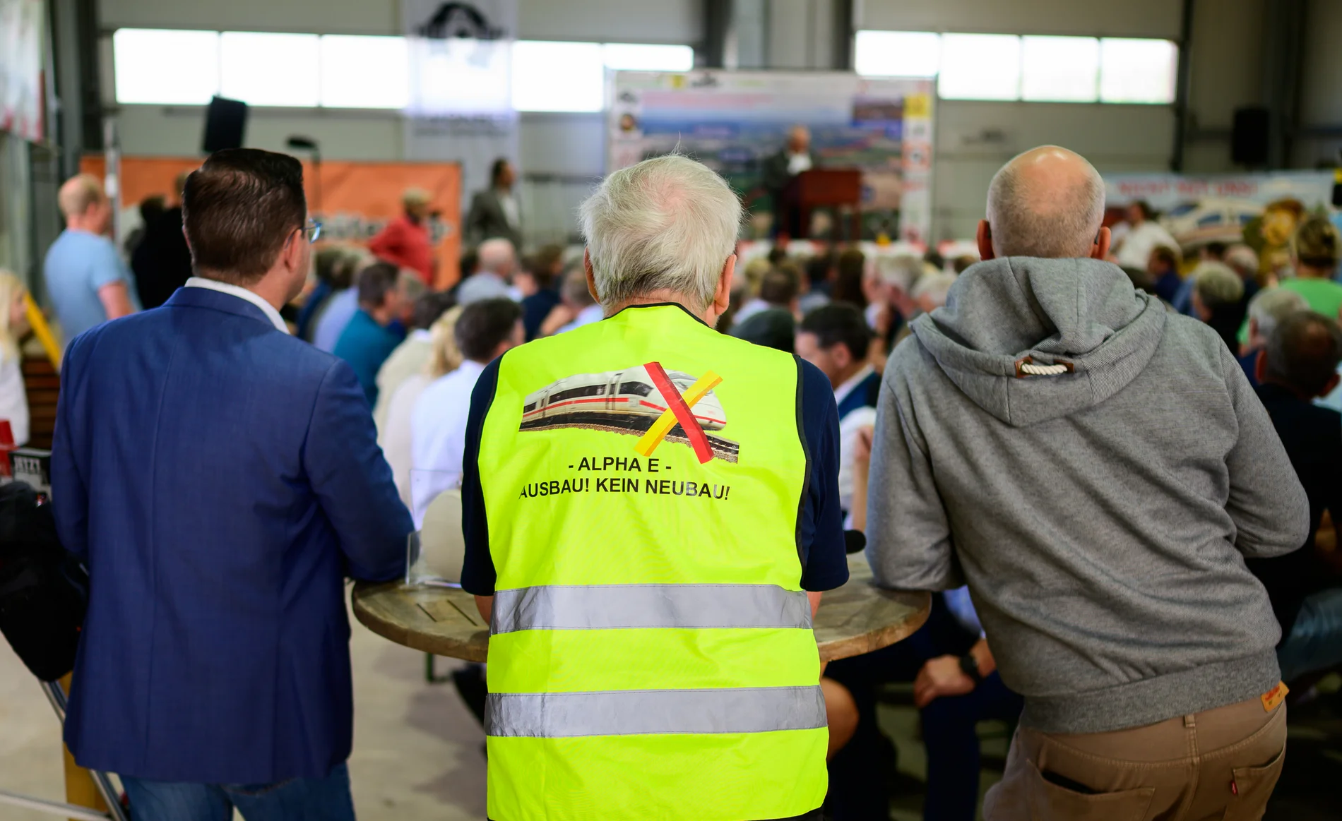 "Alpha E, Ausbau! Kein Neubau" steht auf einer Warnweste eines Mannes